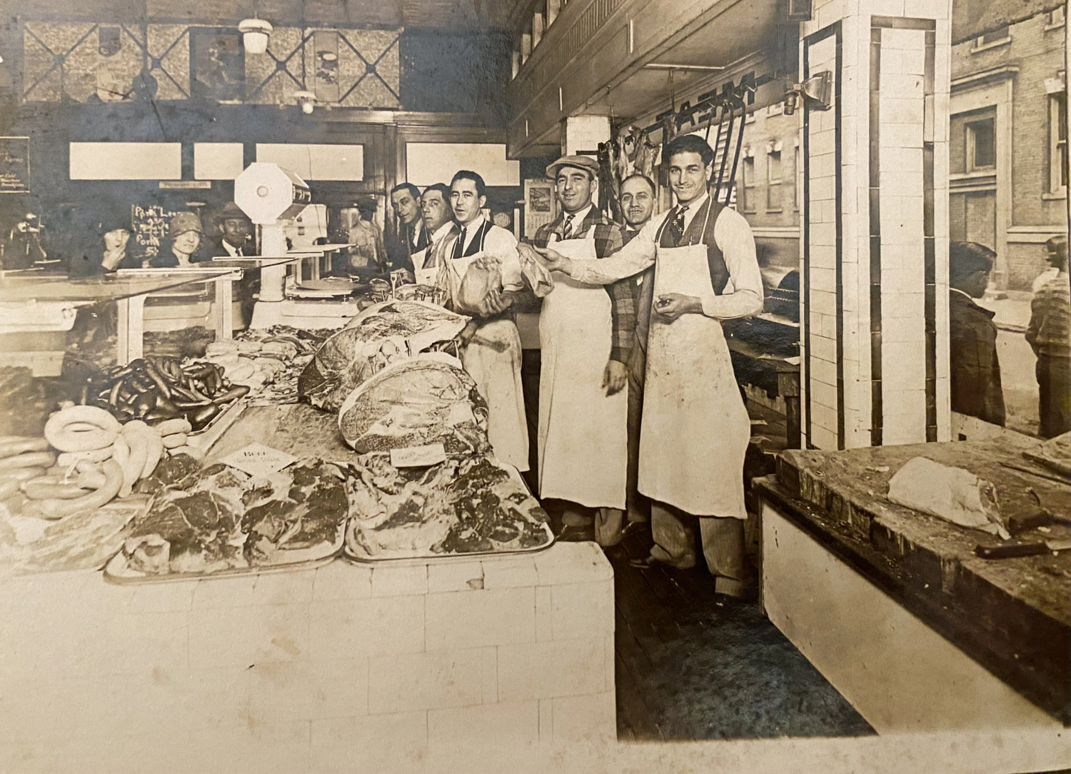 Group of butchers in a city butcher shop holding cuts of meat with meat for sale on the table