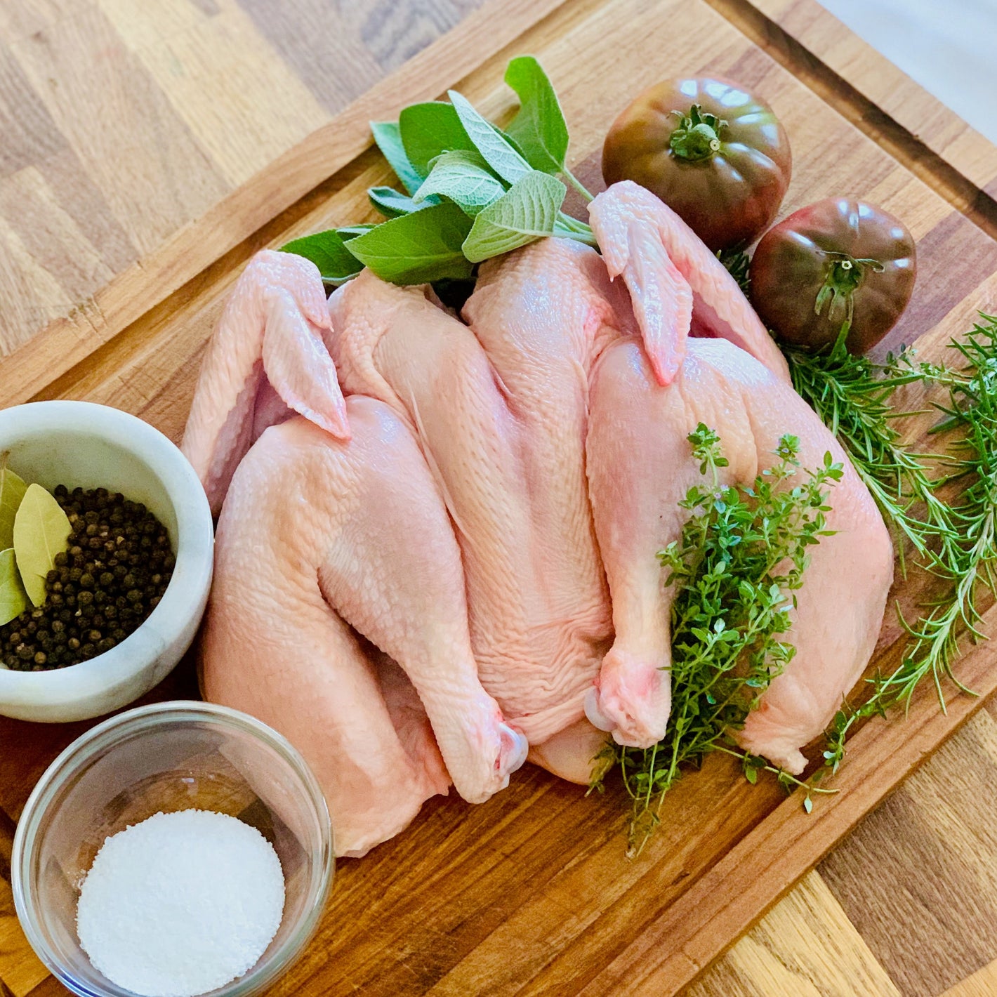 Organic pasture raised spatchcock butterfly chicken for grilling, roasting, with herbs and spices on wood cutting board.